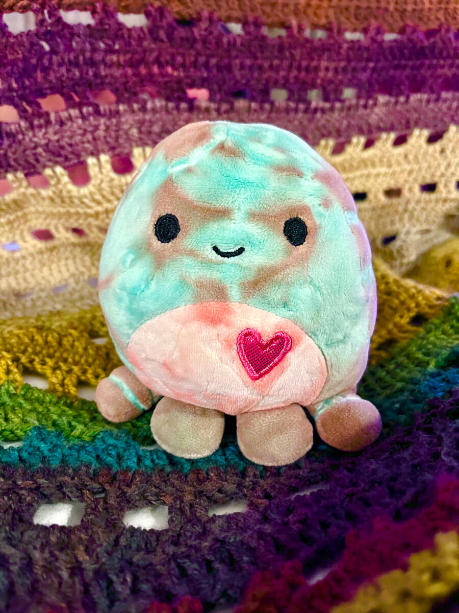 A little stuffed octopus with a heart on its chest sitting on a rainbow background